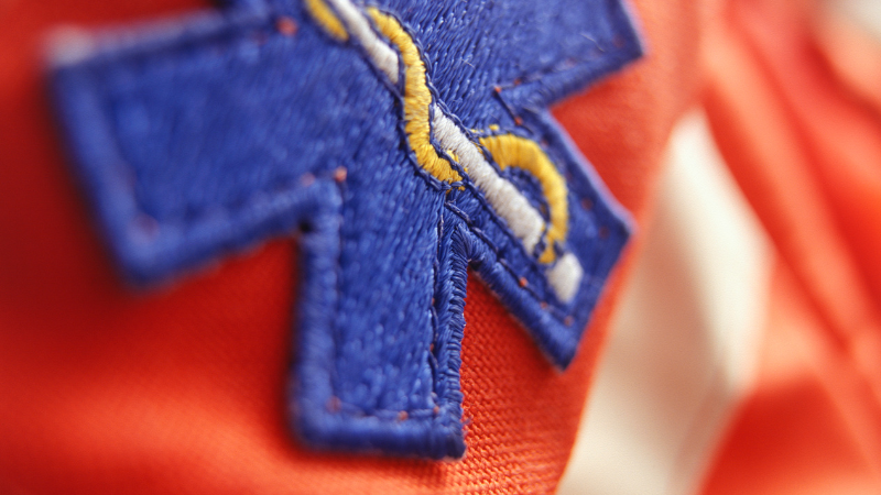 a photo shows an up-close and artistic image of a blue EMT badge on a red-orange canvas background.